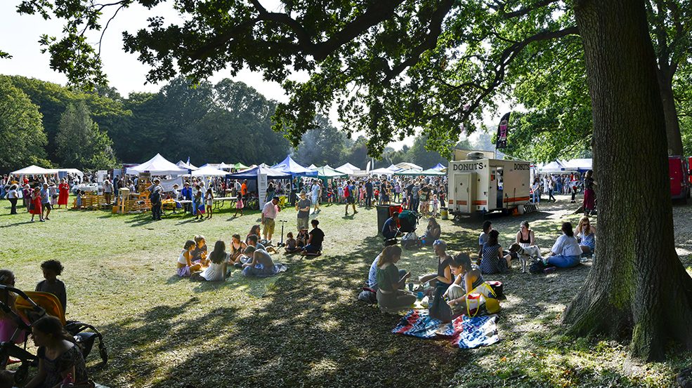 Image of the East Finchley Festival in Cherry Tree Wood, East Finchley, N2 with festival goers and gazeebos.